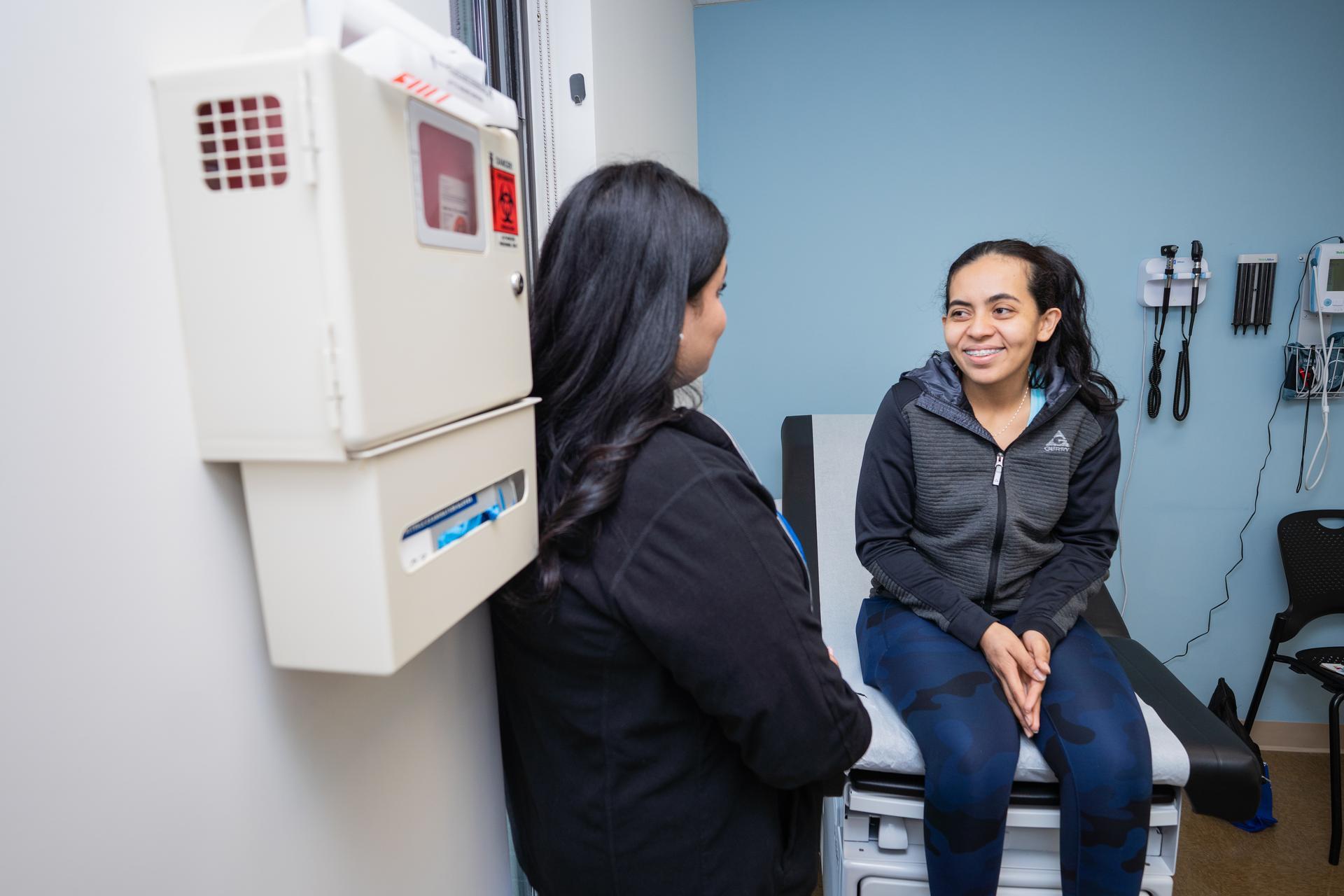 nurse on left in white lab coat stand with arm around patient in an examination room