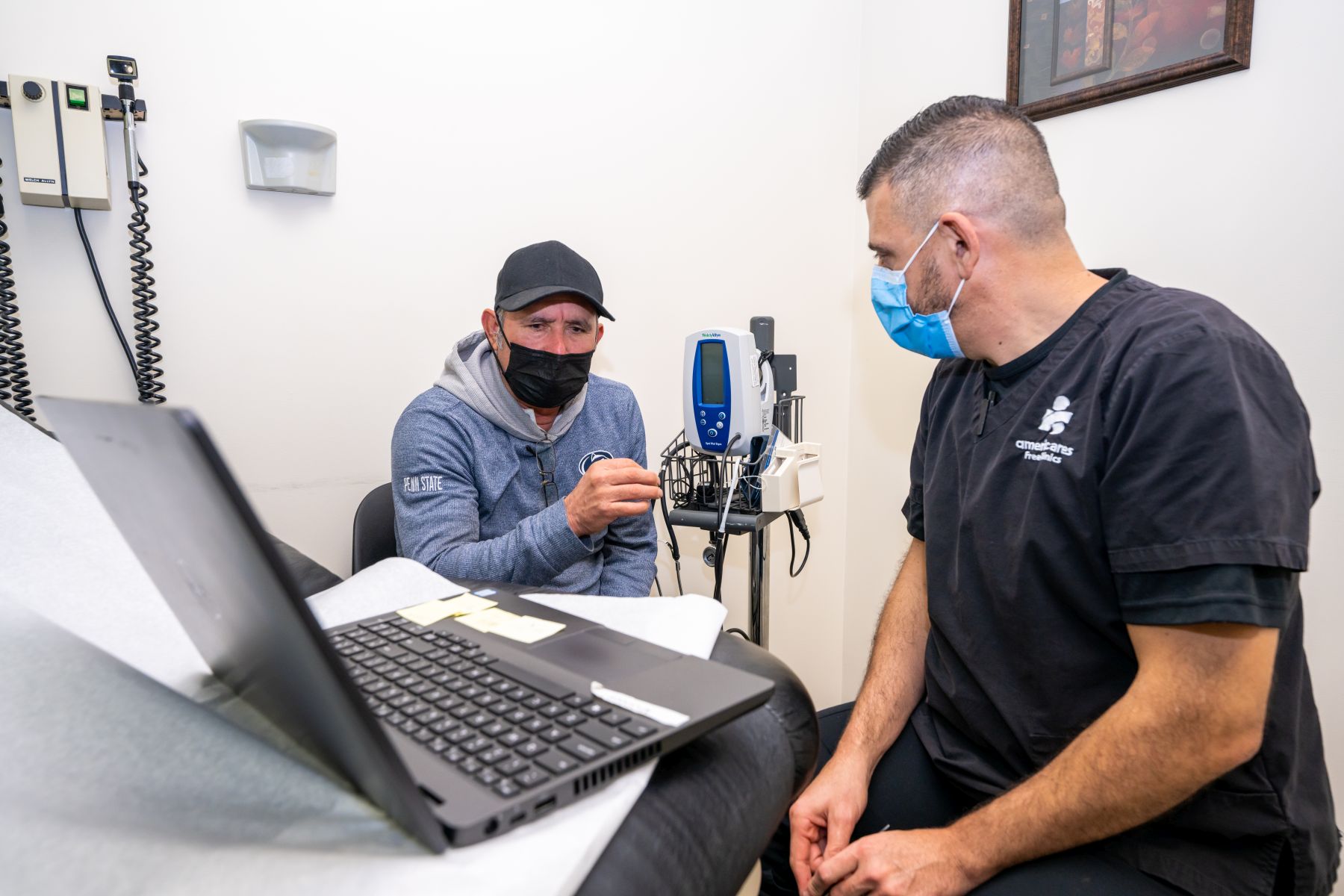 health worker on right in mask speaks with patient in baseball cap and mask on left